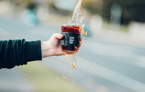 A hand holding a coffee mug. Coffee is pouring into the mug and overflowing.
